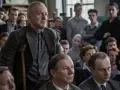 Mężczyzna z laską przemawia do grupy ludzi. Scena z filmów o artystach, gdzie dyskusja o sztuce jest równie ważna jak samo tworzenie.