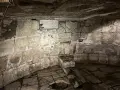 Kamienne wnętrze, przypominające więzienie mamertyńskie, z tablicą upamiętniającą wydarzenia z historii.