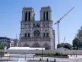 Odbudowa katedry Notre Dame po pożarze. Widoczna fasada, rusztowania, dźwigi i białe namioty.