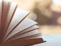 Otwarta księga, jej strony rozchylone jak wachlarz. Widać tekst, numery stron. To jak synkretyzm idei, gdzie różne wątki splatają się w całość.