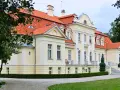 Dawny folwark szlachecki, dziś pałac z czerwoną dachówką, otoczony zielenią i brukowanym podjazdem.