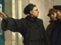 Marcin Luter, z młotkiem w dłoni, przybija swoje 95 tez do drzwi kościoła, rozpoczynając reformację.