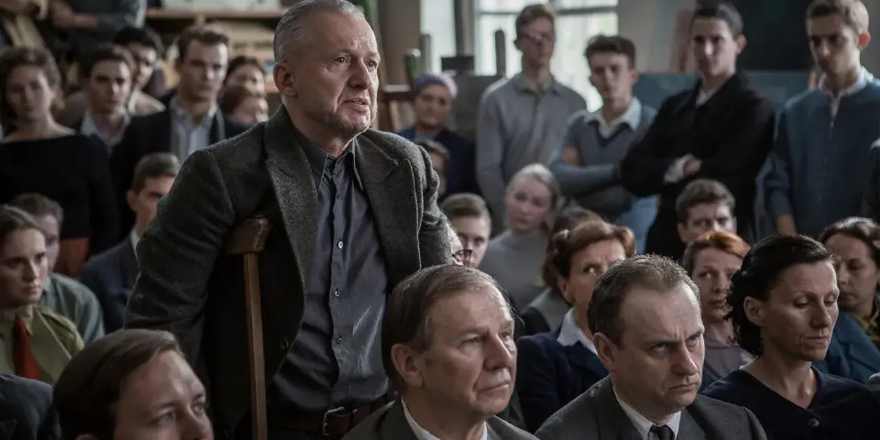 Mężczyzna z laską przemawia do grupy ludzi. Scena z filmów o artystach, gdzie dyskusja o sztuce jest równie ważna jak samo tworzenie.