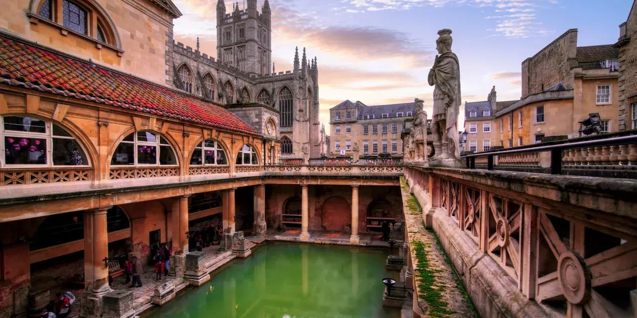 Starożytne łaźnie rzymskie w Bath, z zieloną wodą i zabytkową architekturą, w blasku zachodzącego słońca.