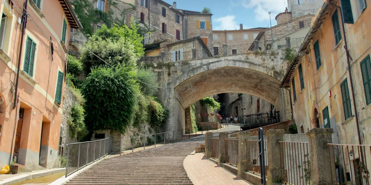 Perugia zwiedzanie: malownicze schody prowadzące pod zabytkowy most, otoczone kamiennymi domami i zielenią.