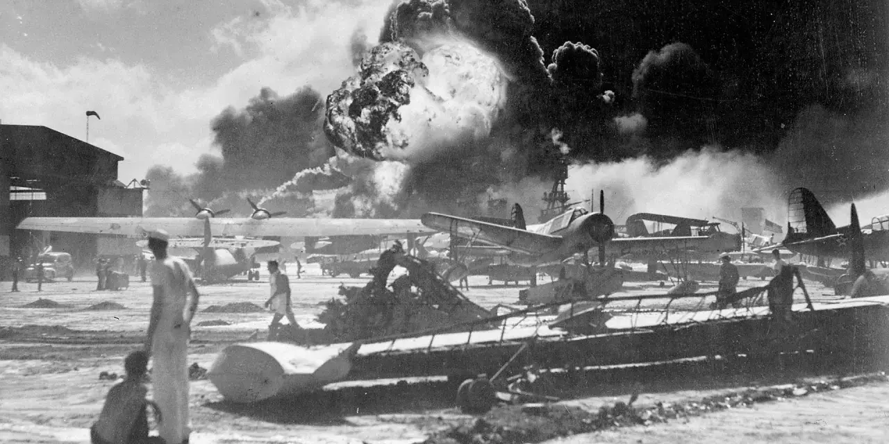 Dramatyczny wybuch w Pearl Harbor. Dym unosi się nad samolotami i budynkami, świadcząc o chaosie ataku.