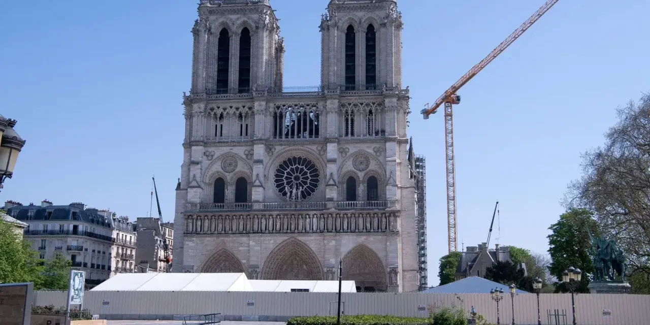Odbudowa katedry Notre Dame po pożarze. Widoczna fasada, rusztowania, dźwigi i białe namioty.