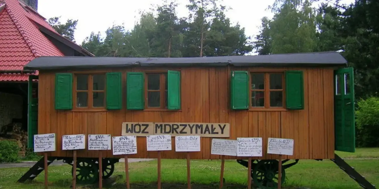 Drewniany wóz drzymały z zielonymi okiennicami i tabliczkami z cytatami.