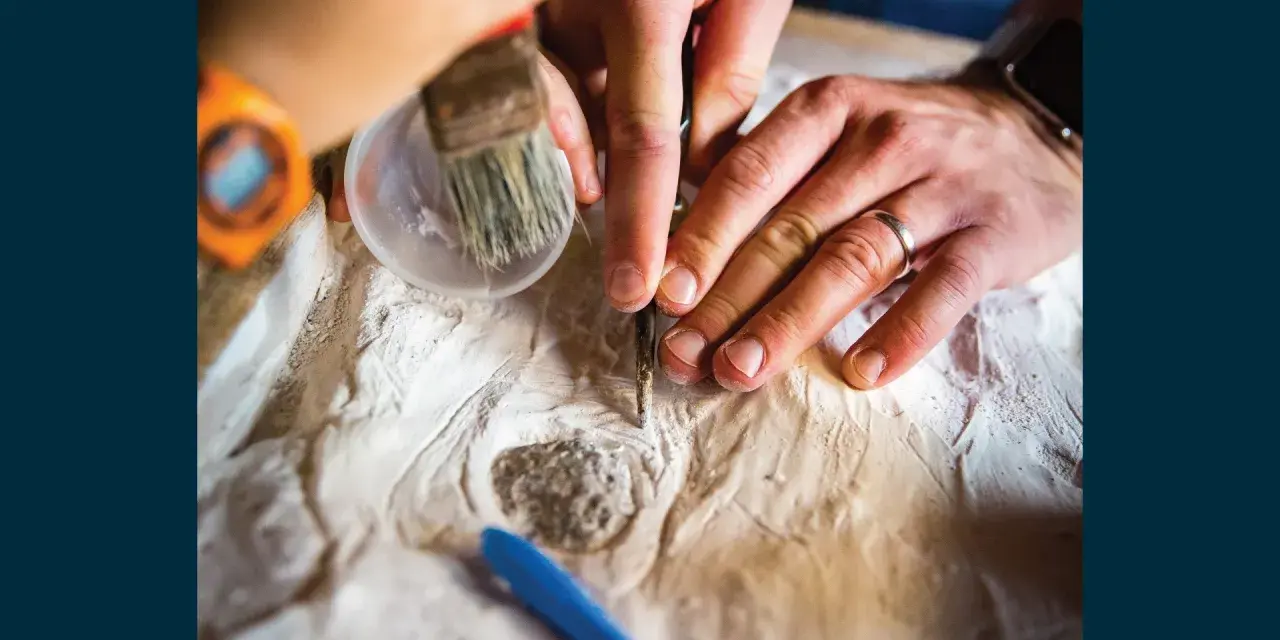 Ręce archeologa i paleontologa delikatnie oczyszczają znalezisko.