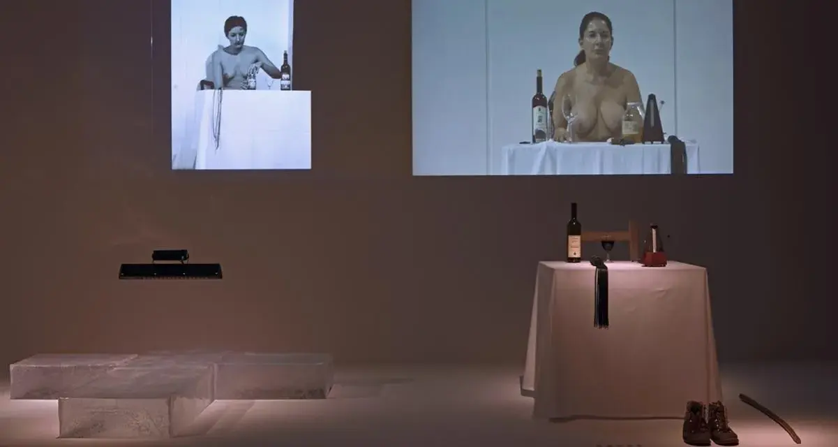 Fragmenty performance'u Mariny Abramović: kobiety przy stołach z winem i przedmiotami, obok instalacja z lodu.