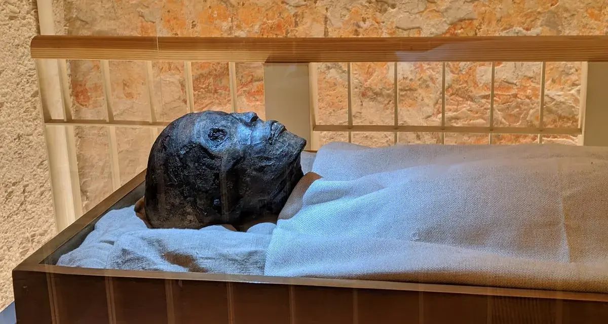 Mumia Tutanchamona spoczywa w szklanej gablocie, owinięta w płótno.