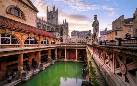 Starożytne łaźnie rzymskie w Bath, z zieloną wodą i zabytkową architekturą, w blasku zachodzącego słońca.