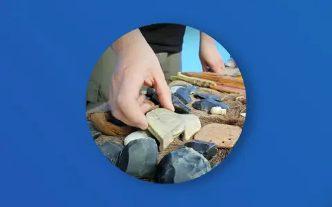 Ręka wybiera kamienną figurkę bizona wśród narzędzi i artefaktów. Zakazana archeologia najnowsze odkrycia.