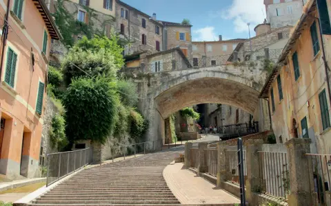 Perugia zwiedzanie: malownicze schody prowadzące pod zabytkowy most, otoczone kamiennymi domami i zielenią.