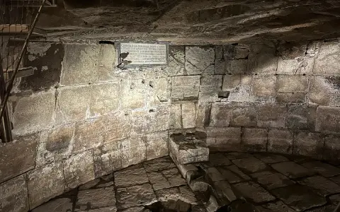 Kamienne wnętrze, przypominające więzienie mamertyńskie, z tablicą upamiętniającą wydarzenia z historii.