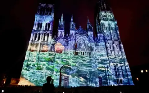 Katedra w Rouen oświetlona projekcjami w kolorach niebieskim i zielonym, z widocznymi żaglówkami.