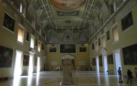 Wnętrze muzeum archeologicznego w Neapolu. Olśniewające sklepienie, obrazy na ścianach i rzeźba w centrum.