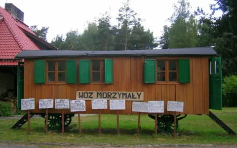 Drewniany wóz drzymały z zielonymi okiennicami i tabliczkami z cytatami.