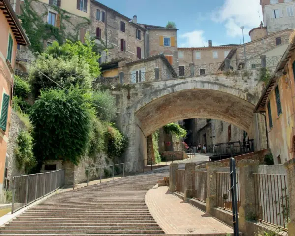 Perugia zwiedzanie: malownicze schody prowadzące pod zabytkowy most, otoczone kamiennymi domami i zielenią.