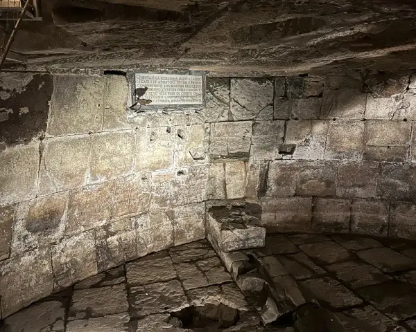 Kamienne wnętrze, przypominające więzienie mamertyńskie, z tablicą upamiętniającą wydarzenia z historii.