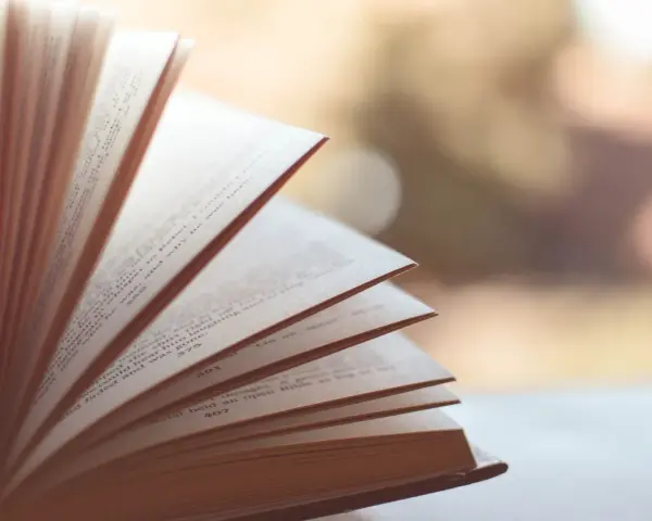 Otwarta księga, jej strony rozchylone jak wachlarz. Widać tekst, numery stron. To jak synkretyzm idei, gdzie różne wątki splatają się w całość.