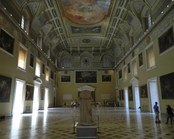 Wnętrze muzeum archeologicznego w Neapolu. Olśniewające sklepienie, obrazy na ścianach i rzeźba w centrum.