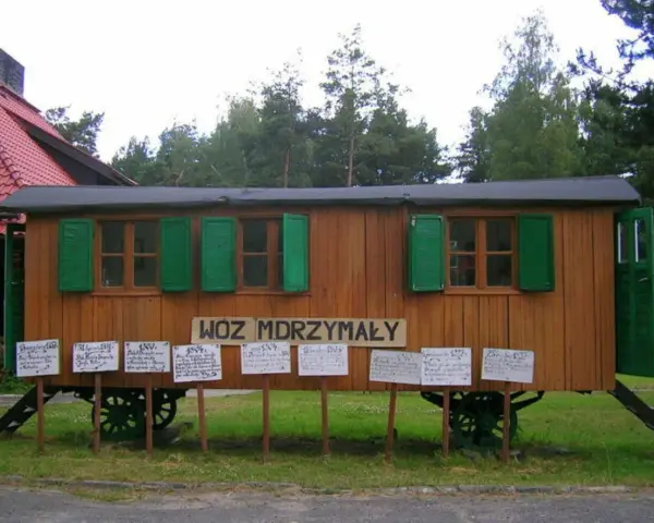 Drewniany wóz drzymały z zielonymi okiennicami i tabliczkami z cytatami.