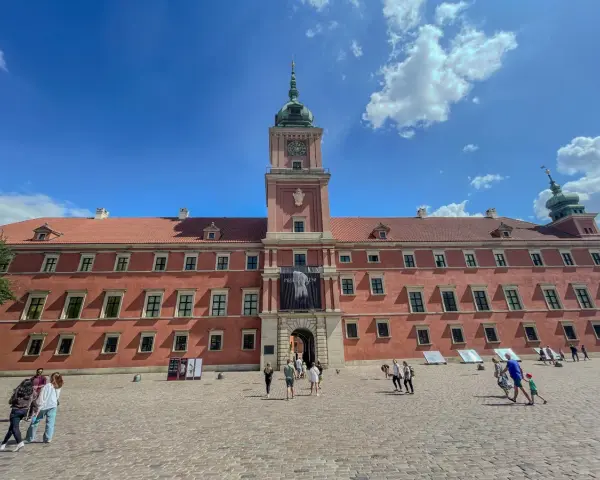 Zwiedzanie Zamku Królewskiego w Warszawie. Tłum turystów na dziedzińcu przed zabytkowym budynkiem.