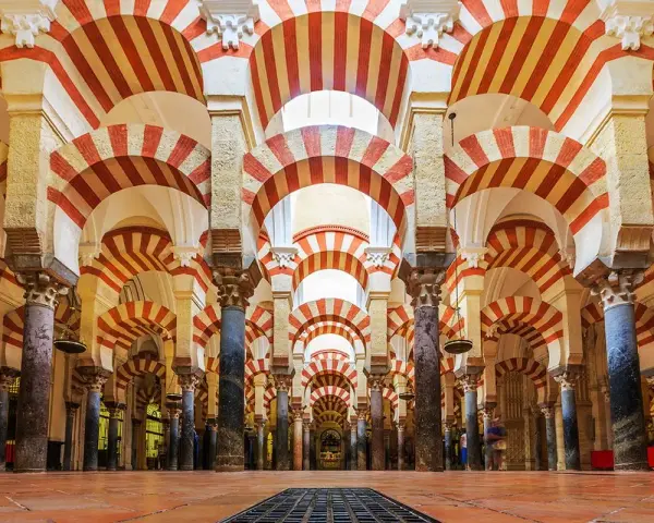 Wnętrze Mezquita w Kordobie z charakterystycznymi łukami w biało-czerwone pasy, tworzącymi hipnotyzujący wzór.