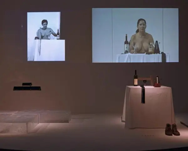 Fragmenty performance'u Mariny Abramović: kobiety przy stołach z winem i przedmiotami, obok instalacja z lodu.