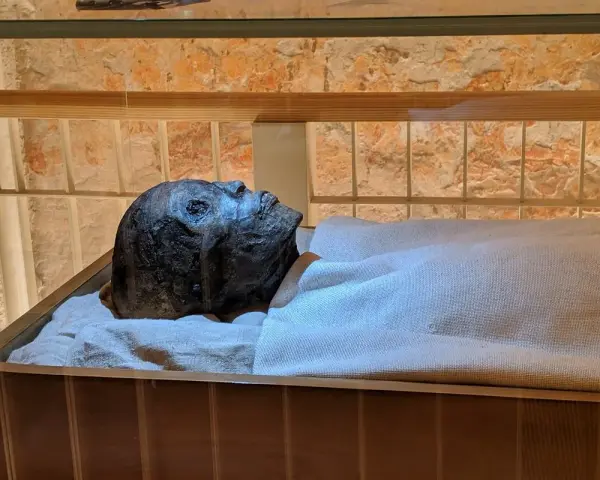 Mumia Tutanchamona spoczywa w szklanej gablocie, owinięta w płótno.