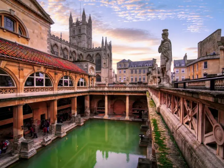 Starożytne łaźnie rzymskie w Bath, z zieloną wodą i zabytkową architekturą, w blasku zachodzącego słońca.