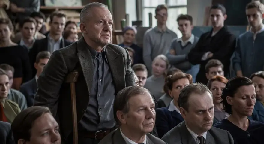 Mężczyzna z laską przemawia do grupy ludzi. Scena z filmów o artystach, gdzie dyskusja o sztuce jest równie ważna jak samo tworzenie.