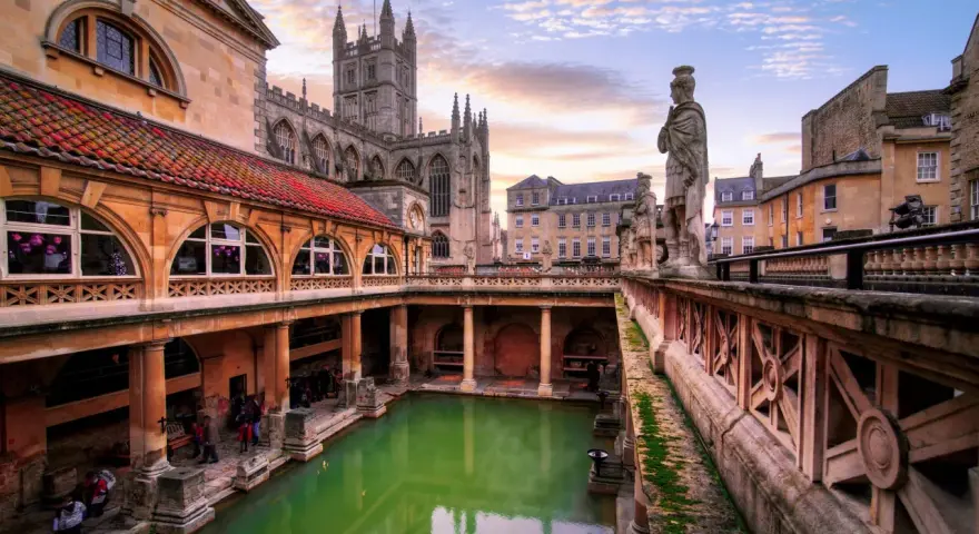Starożytne łaźnie rzymskie w Bath, z zieloną wodą i zabytkową architekturą, w blasku zachodzącego słońca.