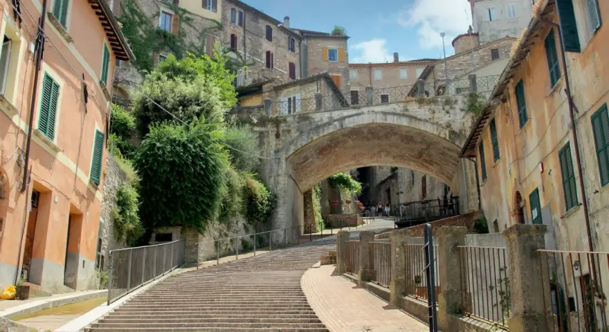 Perugia zwiedzanie: malownicze schody prowadzące pod zabytkowy most, otoczone kamiennymi domami i zielenią.
