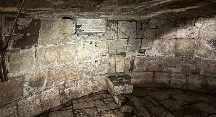 Kamienne wnętrze, przypominające więzienie mamertyńskie, z tablicą upamiętniającą wydarzenia z historii.