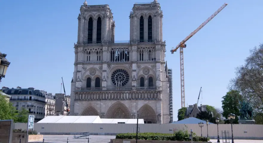 Odbudowa katedry Notre Dame po pożarze. Widoczna fasada, rusztowania, dźwigi i białe namioty.