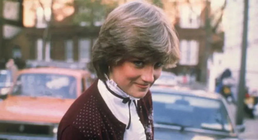 Młoda Diana Spencer, zanim została księżną, w bordowym sweterku i białej bluzce. Jej arystokratyczne pochodzenie widać w subtelnych gestach.