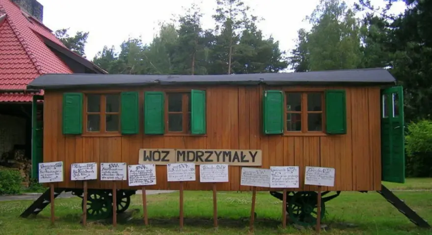 Drewniany wóz drzymały z zielonymi okiennicami i tabliczkami z cytatami.