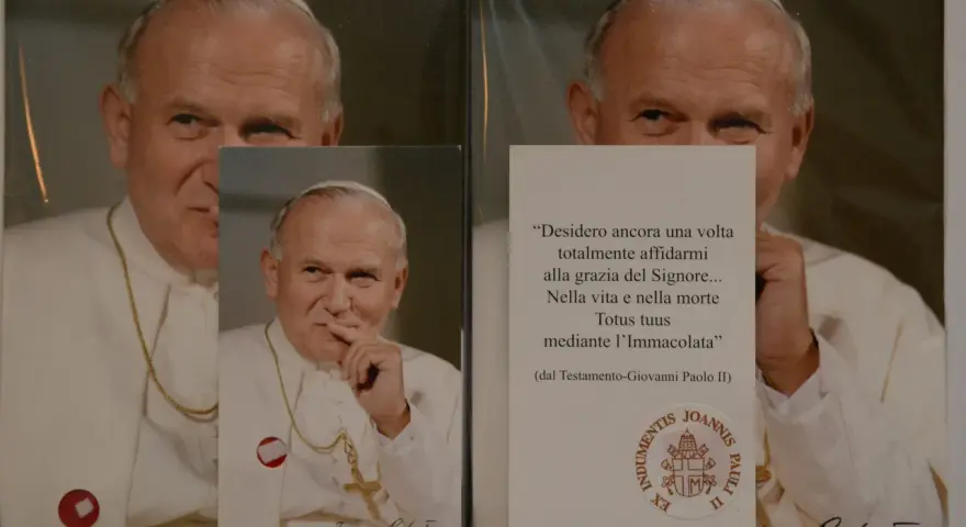 Relikty Jana Pawła II. Na zdjęciu papież w białej szacie, z krzyżem na szyi. Obok cytat z jego testamentu.
