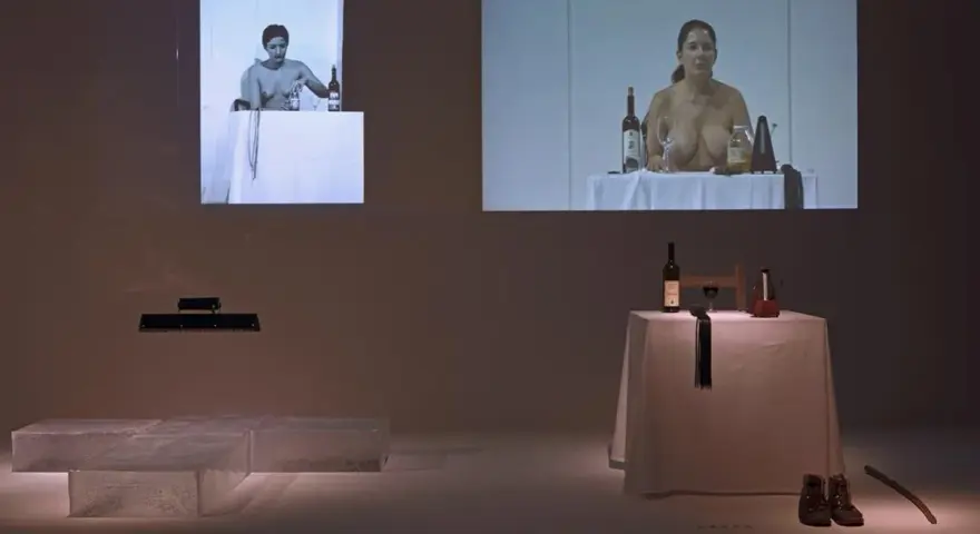 Fragmenty performance'u Mariny Abramović: kobiety przy stołach z winem i przedmiotami, obok instalacja z lodu.