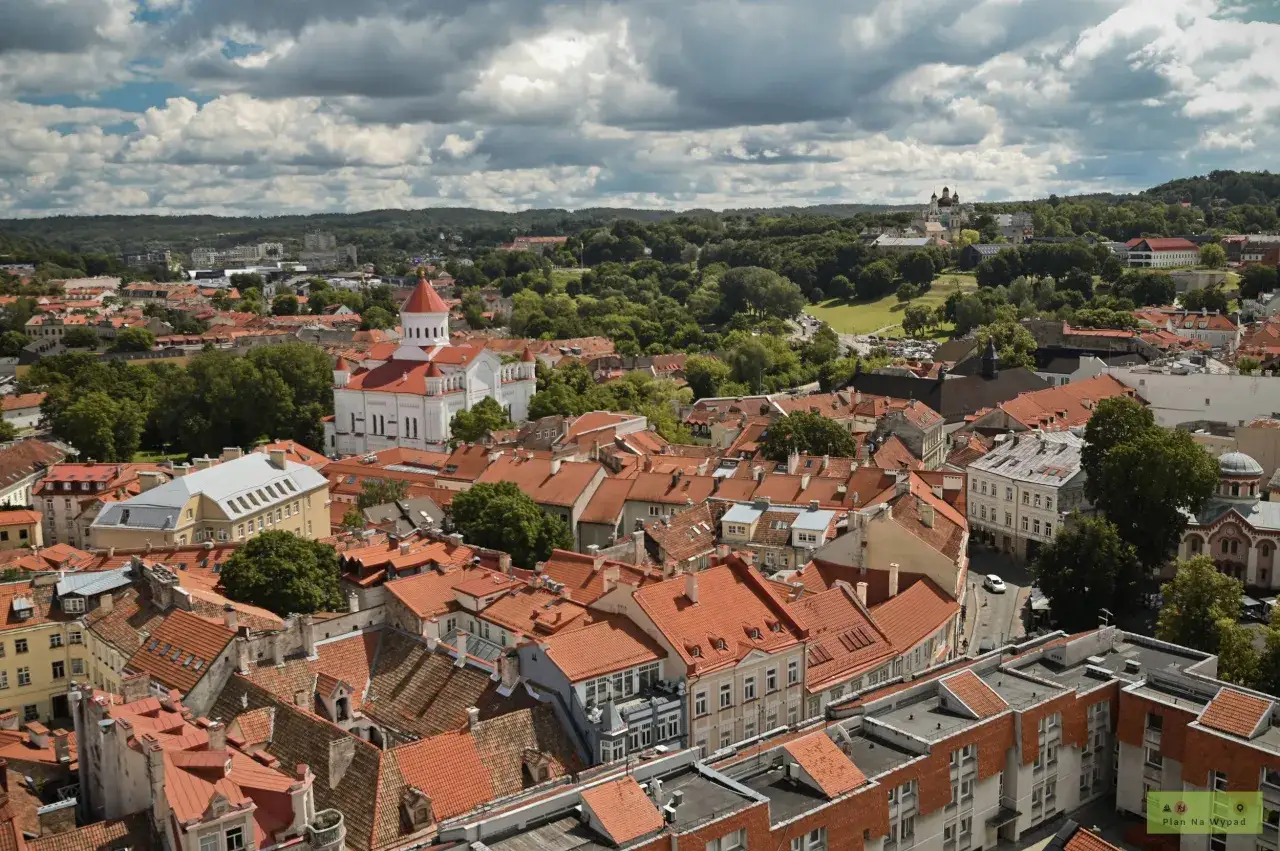 Widok na dachy Wilna, w tym białą cerkiew z czerwoną kopułą. W oddali zielone wzg&oacute;rza i budynki. Idealne miejsce, by zobaczyć, co warto zobaczyć w Wilnie.