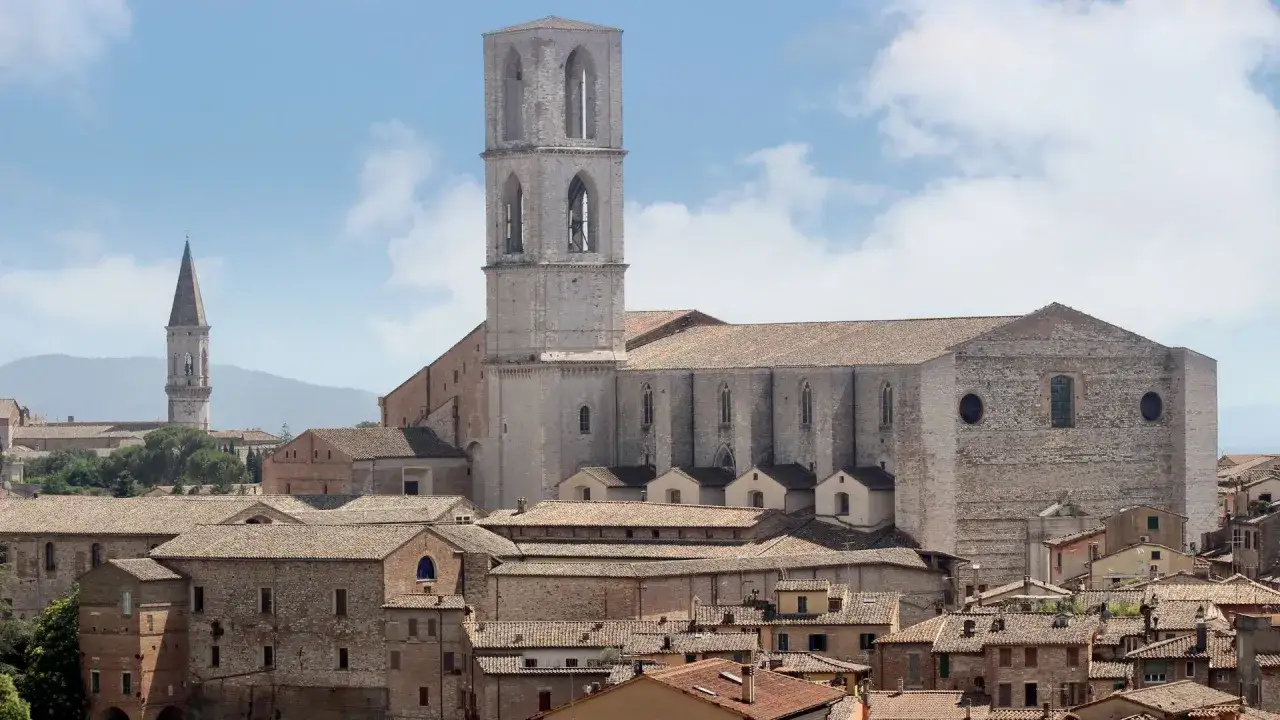 Perugia zwiedzanie: imponująca katedra z wieżą i inne zabytkowe budynki na tle wzgórz.
