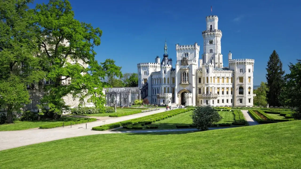 Majestatyczne zamki Czech, biały zamek Hlubok&aacute; otoczony zielonym ogrodem, pod błękitnym niebem.