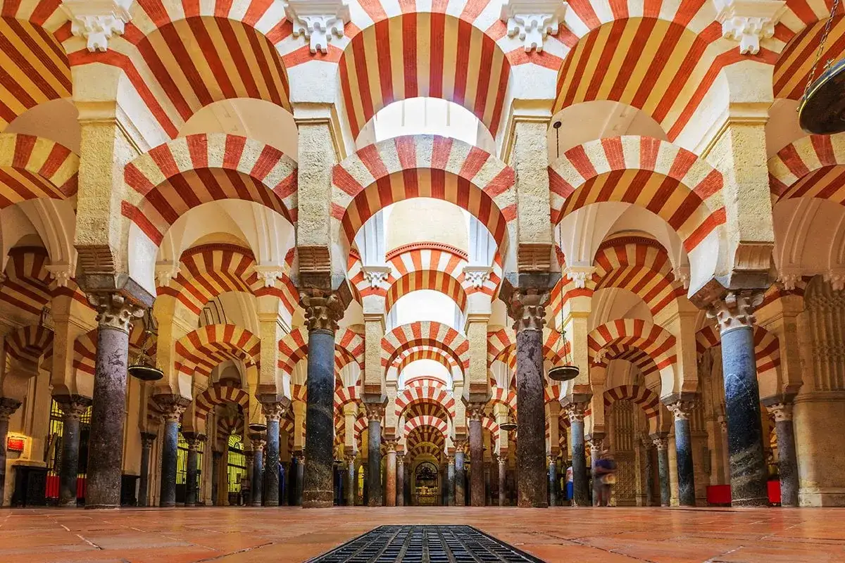 Wnętrze Mezquita w Kordobie zachwyca rzędami łuk&oacute;w w charakterystyczne czerwono-białe pasy, tworząc hipnotyzujący labirynt.