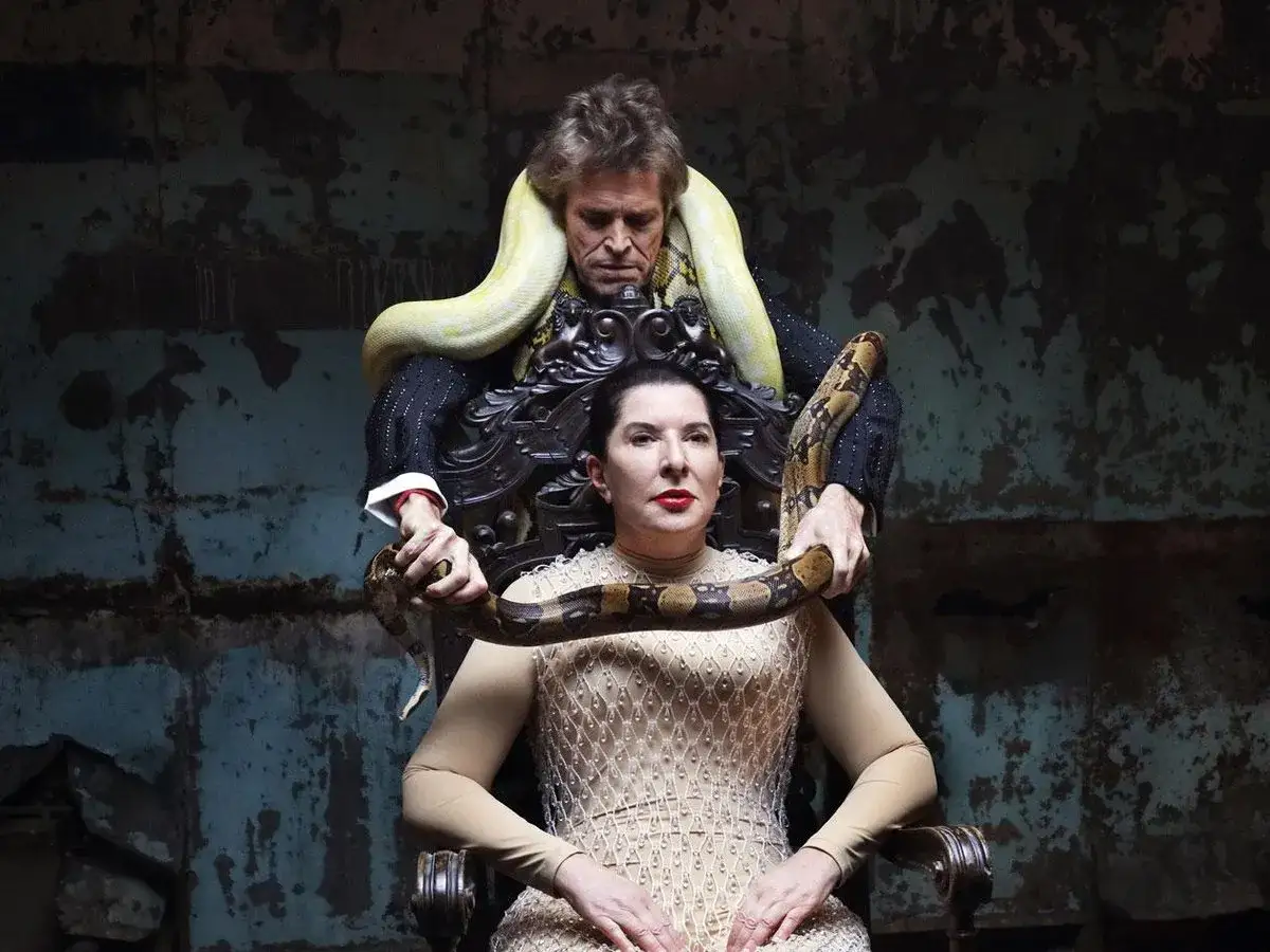 Marina Abramović performance: kobi siedzi na tronie, a mężczyzna z wężami wok&oacute;ł szyi i ramion trzyma jednego z nich na jej rękach.