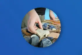Ręka wybiera kamienną figurkę bizona wśród narzędzi i artefaktów. Zakazana archeologia najnowsze odkrycia.