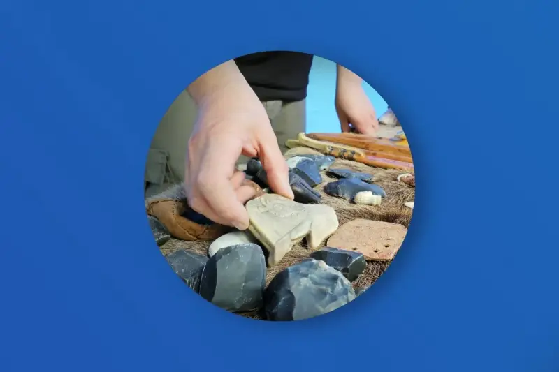 Ręka wybiera kamienną figurkę bizona wśród narzędzi i artefaktów. Zakazana archeologia najnowsze odkrycia.