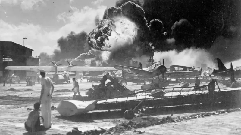 Dramatyczny wybuch w Pearl Harbor. Dym unosi się nad samolotami i budynkami, świadcząc o chaosie ataku.